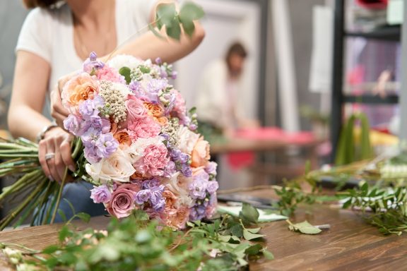 Thats handy! A person arranging a bouquet of pink and purple flowers on a table.