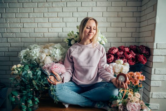 Just chill....... A woman sits cross-legged among various colourful flowers, smiling peacefully.