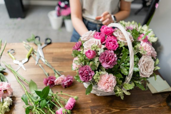 Basket of flowers Floral arrangement in a basket with various pink and cream flowers on a wooden table.