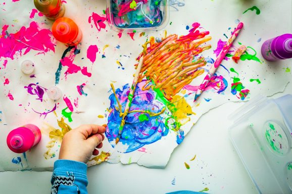 A splash of colour Colourful artwork created with various paints and tools, with a hand in the foreground.